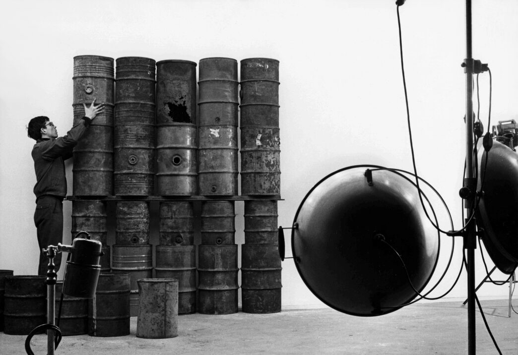 Christo during the erection of "26 Oil Barrels (1961)" in the studio of photographer Jean-Dominique Lajoux Paris, 1961