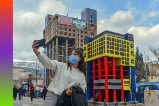 A selfie being taken in front of the cake model of a governmental building in Kahramanmaraş. The building, known as “the ugliest building in the World,” was demolished in 2022 due to its unattractive appearance. © DHA. Pavilion of Türkiye.